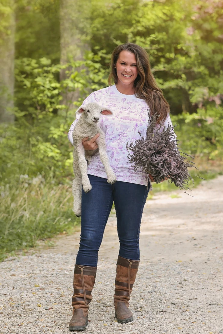 Woman holding a lamb and a bundle of dried plants on a path in a natural setting